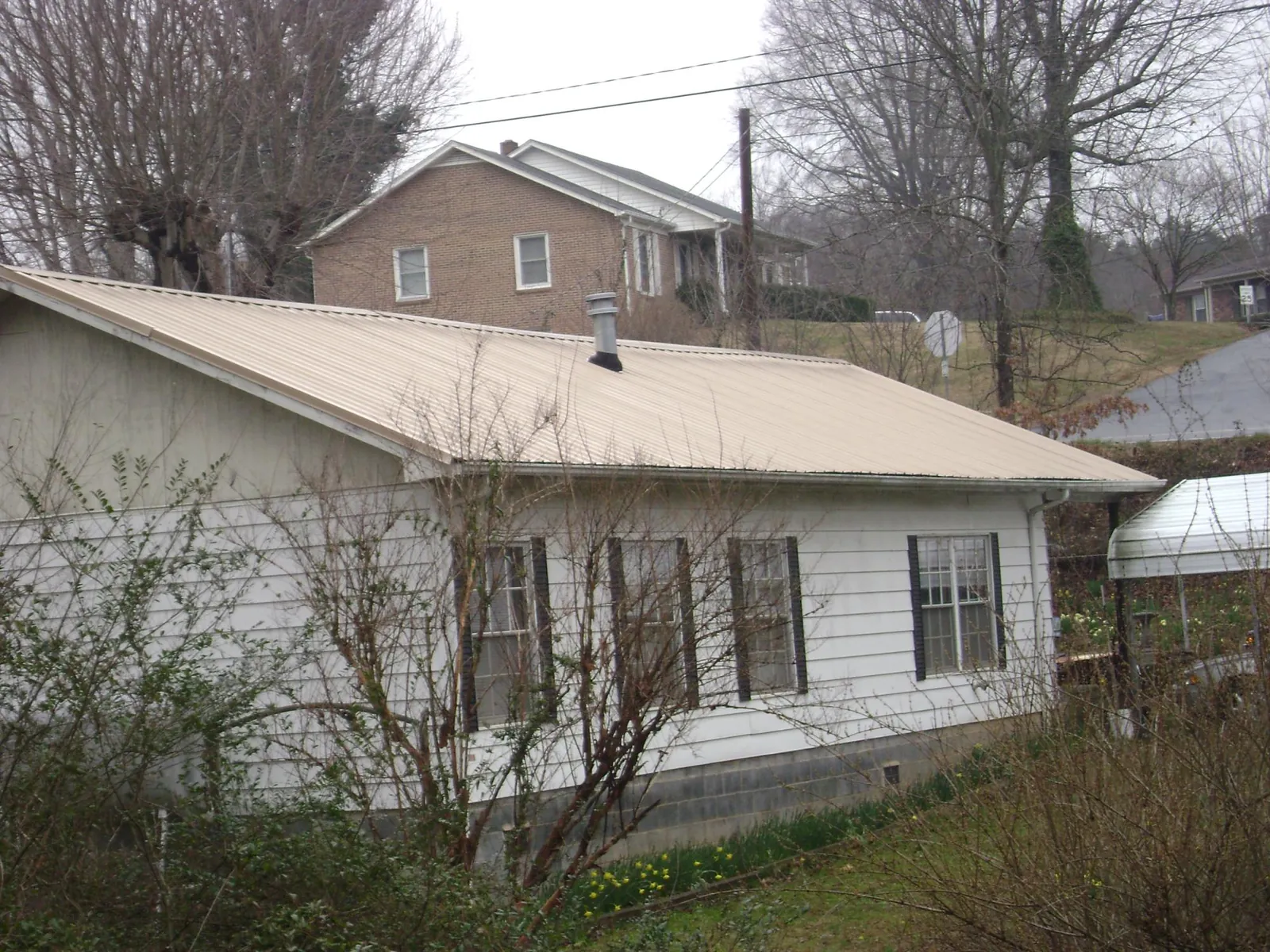 Tan metal roof on a white sided house set into a hillside — Commercial Roofing by Roofing Brothers in Bluffton
